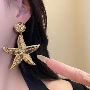 Oversized textured gold starfish drop earrings shown worn on ear for detail view