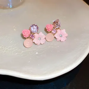 Close-up detail of pink flower stud earrings featuring purple crystals and resin