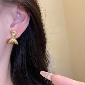 Detalle de un elegante pendiente de botón dorado con forma de cola de sirena en modelo