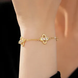 Detail view of a gold clover charm bracelet with zircon stones worn on a delicate wrist