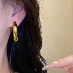 Detalle de pendiente de aro dorado irregular vintage con acabado metálico liso