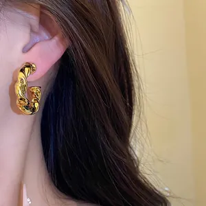 Detalle de un elegante pendiente de aro irregular retorcido dorado en la oreja del modelo
