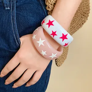 Close-up of chunky resin bangles featuring vibrant drip oil star patterns on model