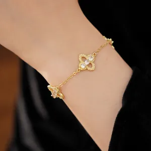 Macro shot of a delicate gold bracelet featuring hollow clover charms with zircons