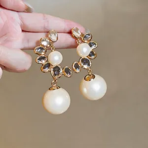 Elegant French vintage style pearl earrings with crystal accents, held in hand for display.