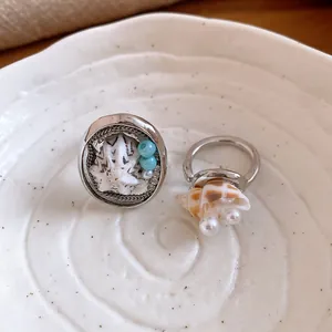 Dettaglio di un anello regolabile con conchiglia e perle su un piatto di ceramica