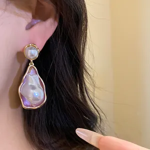 Close-up of vintage gold-tone earrings with irregular pearl pendants on ear