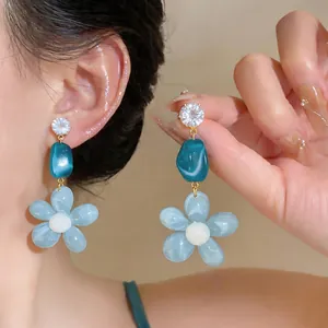 Close-up of blue resin flower earrings with zircon studs and teal beads.