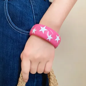 Close-up view of a pink resin bangle featuring white star patterns worn on a model's wrist