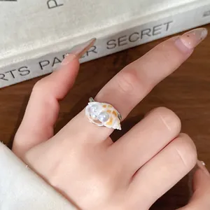 Vista dettagliata di un anello a conchiglia minimalista con perle su un dito umano.