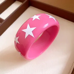 Close-up detail of a pink resin bangle with white enamel star patterns in a display box.