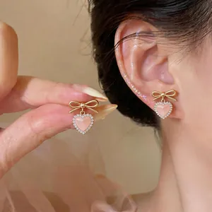 Elegant pink cat-eye heart stud earrings with gold bow and sparkling stones on model