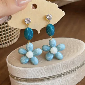Close-up of light blue resin flower earrings with zircon studs and teal beads