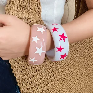 Pair of glossy resin bangles with star patterns on a wrist near a woven bag.