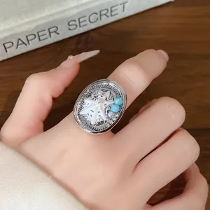 Primo piano di un anello minimalista color argento con dettagli in conchiglia e turchese.
