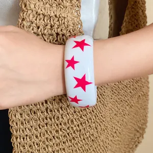 Close-up detail of a white resin bangle featuring vibrant pink star patterns on wrist
