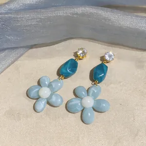 Close-up of flower earrings with teal resin beads and sparkling zircon studs
