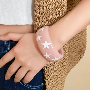 Close-up detail of a stylish pink resin bangle with white star patterns on a model's wrist.
