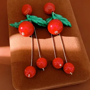 Primo piano di orecchini a ciliegia in resina rossa con foglie verdi e nappe argentate.