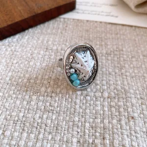 Primo piano di un anello a conchiglia vintage con perline turchesi su sfondo di lino.