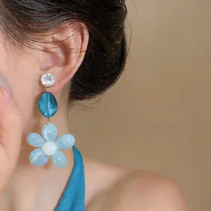 Detailed view of blue resin flower earrings with a sparkling zircon stud on an Asian model