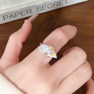 Dettaglio ravvicinato di un delicato anello a conchiglia con perle indossato sul dito