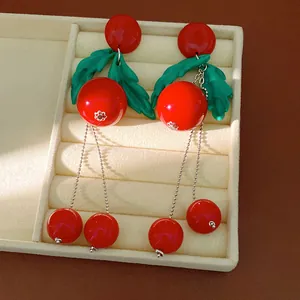 Orecchini in resina rossa con foglie verdi e lunghe nappe a catena in un vassoio per gioielli.