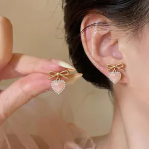 Close-up of sweet pink cat-eye heart earrings with golden bow and rhinestones