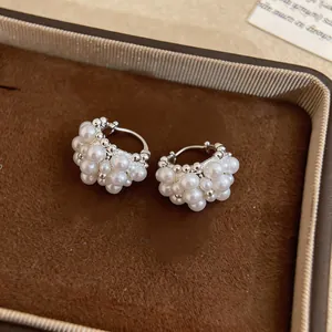 Dettaglio di eleganti orecchini a cerchio con grappolo di perle bianche in scatola