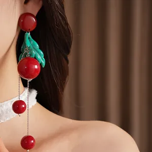 Primo piano di orecchini a forma di ciliegia con perline rosse e foglie verdi su modella