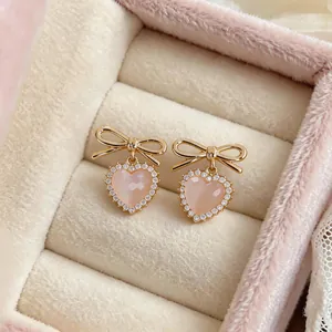 Close-up of elegant pink heart earrings with gold bow-knot and sparkling cz crystals.