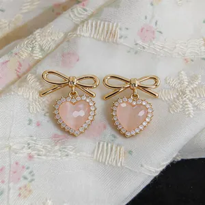 Exquisite close-up of pink heart-shaped stud earrings with golden bowknots and crystals