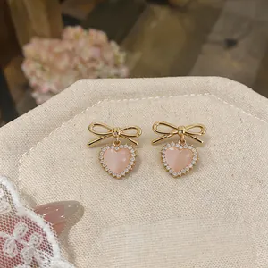 Close-up of pink heart-shaped earrings with gold bows and rhinestone detail.