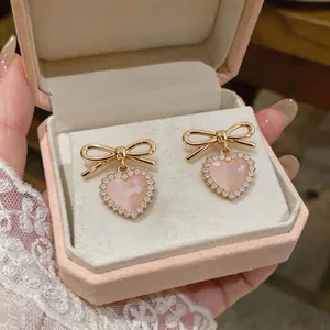 Elegant gold-tone bow and pink heart cat-eye stone earrings shown inside a velvet jewelry box