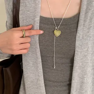 Detailed view of a dainty gold hollow heart pendant necklace worn on a grey cardigan.