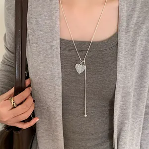 Detailed view of dainty hollow heart lariat necklace worn over a stylish grey cardigan
