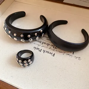 Close-up of black resin cuff bracelets and matching rivet ring on elegant textured prop paper.