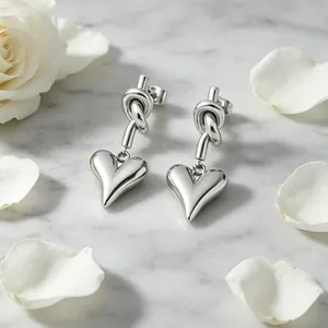 Close-up detail of elegant silver-tone knot and heart drop earrings on marble surface