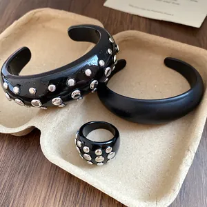 Close-up detail of black resin bangles and a matching ring with silver metal studs in a paper tray