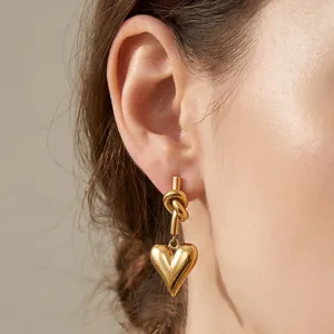 Detailed close-up view of a gold-toned knotted heart drop earring on a model's ear