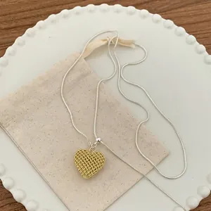 Detail of a gold hollow heart pendant on a silver snake chain with a linen pouch.