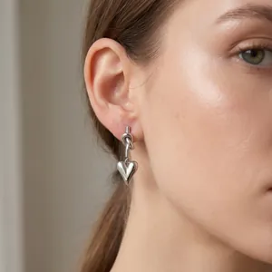 Close-up of high-quality minimalist stainless steel knotted heart earrings worn by a model