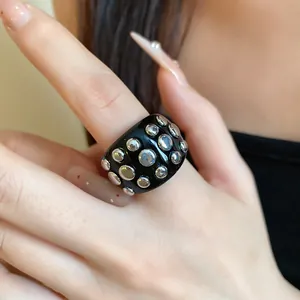 Detail view of black resin ring with silver metal studs on manicured hand