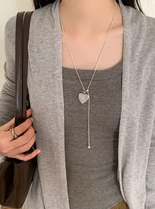 Close-up of a stylish silver hollow heart pendant necklace worn over a grey outfit