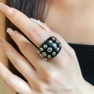 Close-up of a chunky black resin ring with polished silver circular studs.
