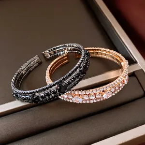 Detalle de brazaletes elásticos multicapa con diamantes de imitación en negro y oro rosa