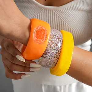 Detail view of chunky resin bangles in vibrant orange, yellow, and glitter styles.