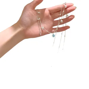 Silver-tone layered necklace with pearls and blue stone pendant, hand-held on white background