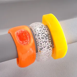 Detailed view of colorful resin irregular geometric bangles in orange, clear glitter and yellow.