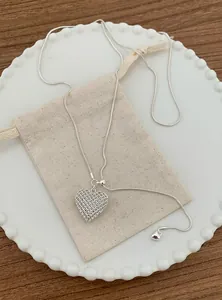 Close-up of a silver-tone hollow heart mesh pendant necklace on a beige gift pouch